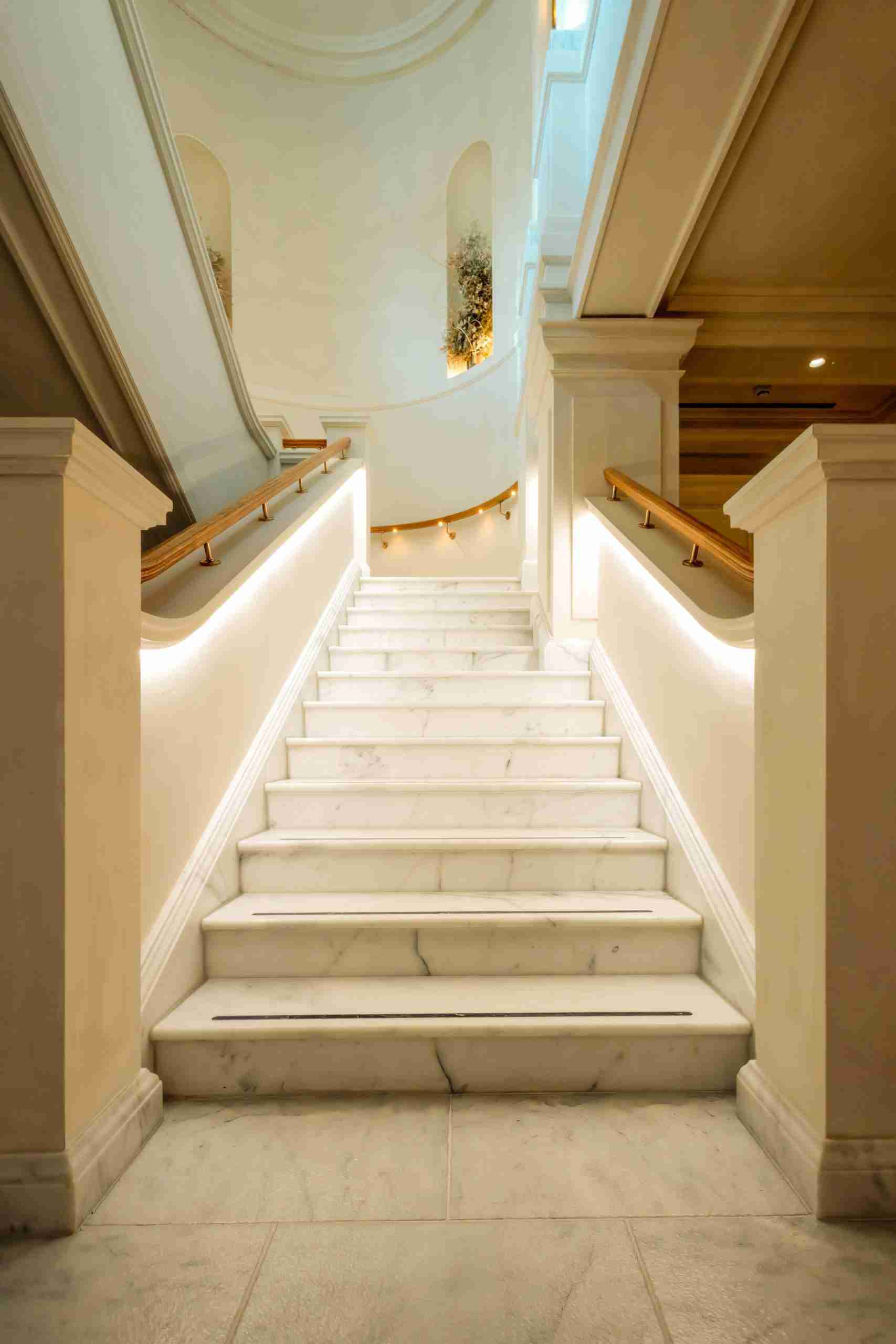 Grand marble staircase featuring custom made bespoke oak handrails and warmed with soft LED lighting.