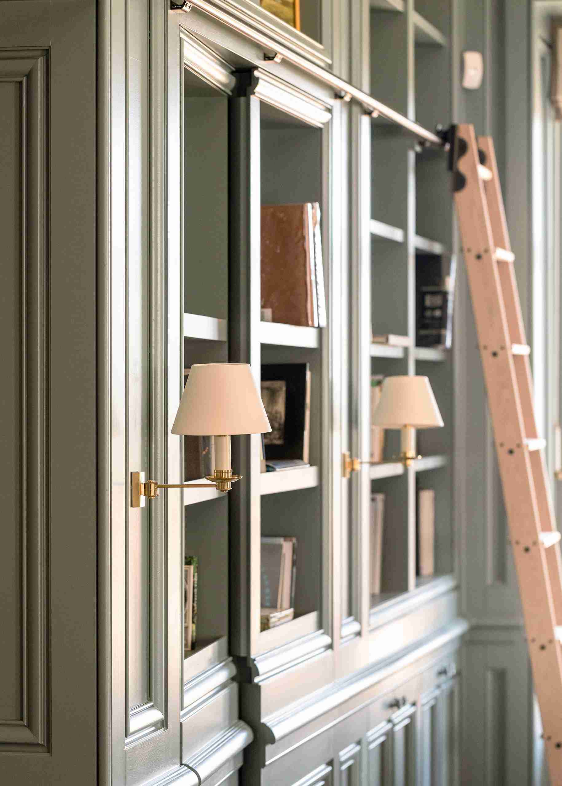 Close-up of bespoke painted built-in library bookshelves with rolling ladder and brass sconces.