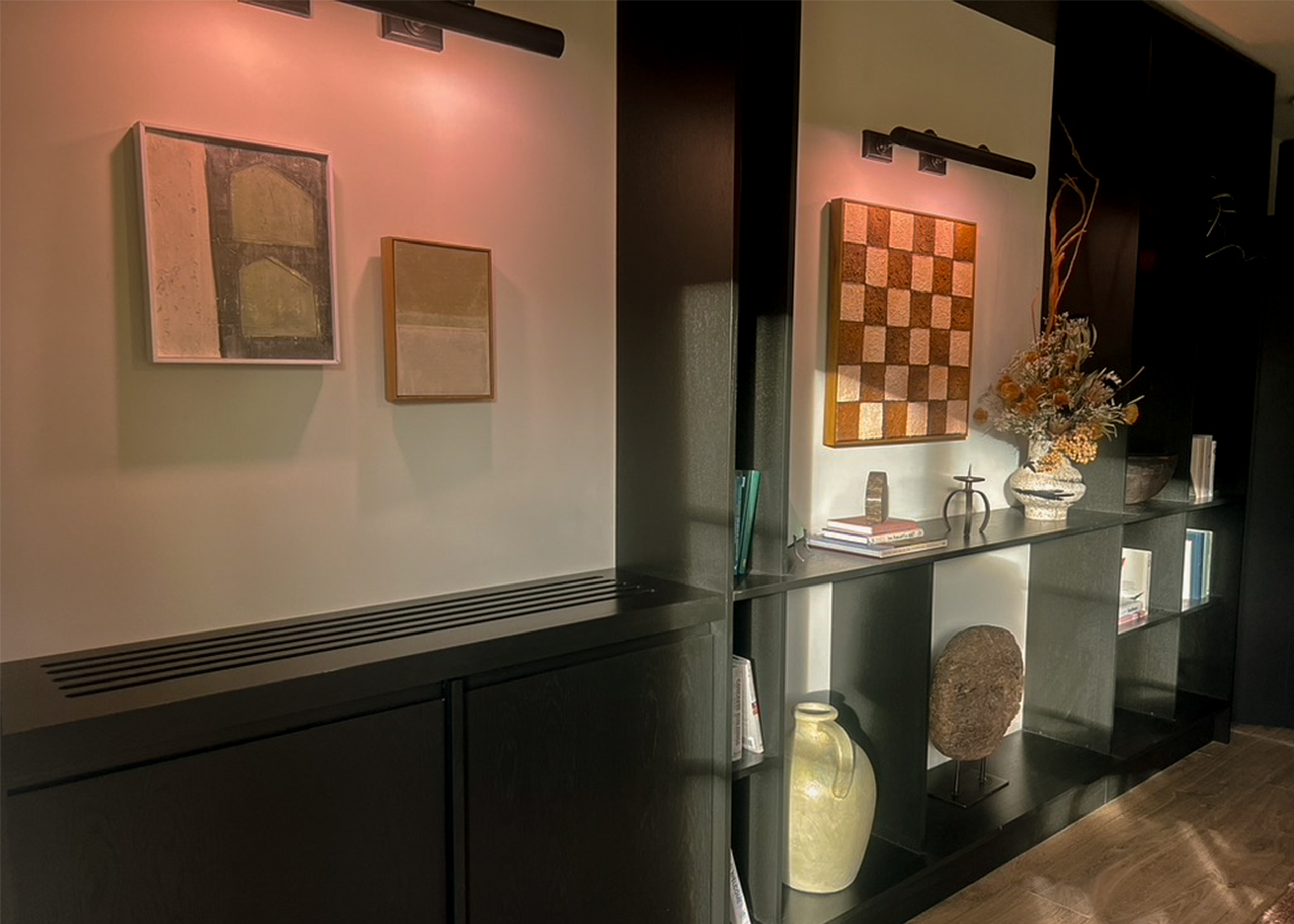Dark and modern cabinetry until with mounted images lit with down lights and features neutral decor