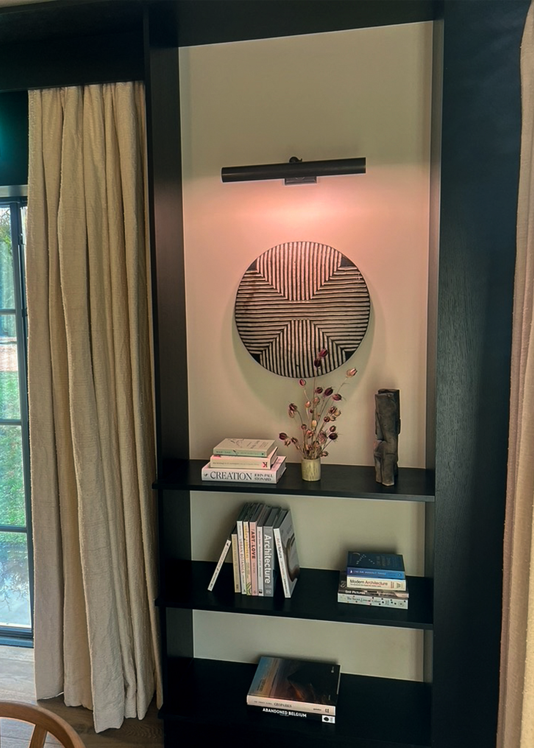 Black shelving unit with natural and synthetic lighting featuring books and a window.